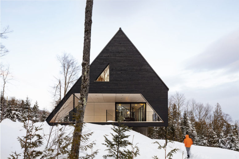 This dramatic A frame cabin is located in the woods on a steep slope and is clad with dark wood