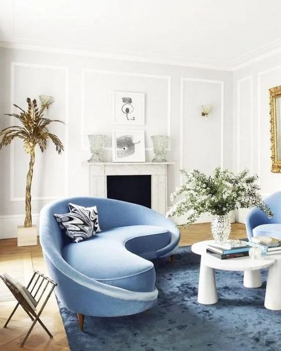 a charming living room with a curved blue sofa and matching chairs and a bold table that catch an eye