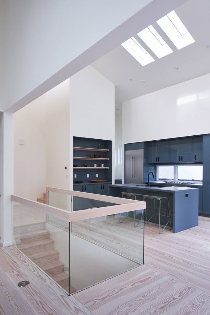 The kitchen is done minimal, with grey cabinets, with built-in shelves and a glass railing