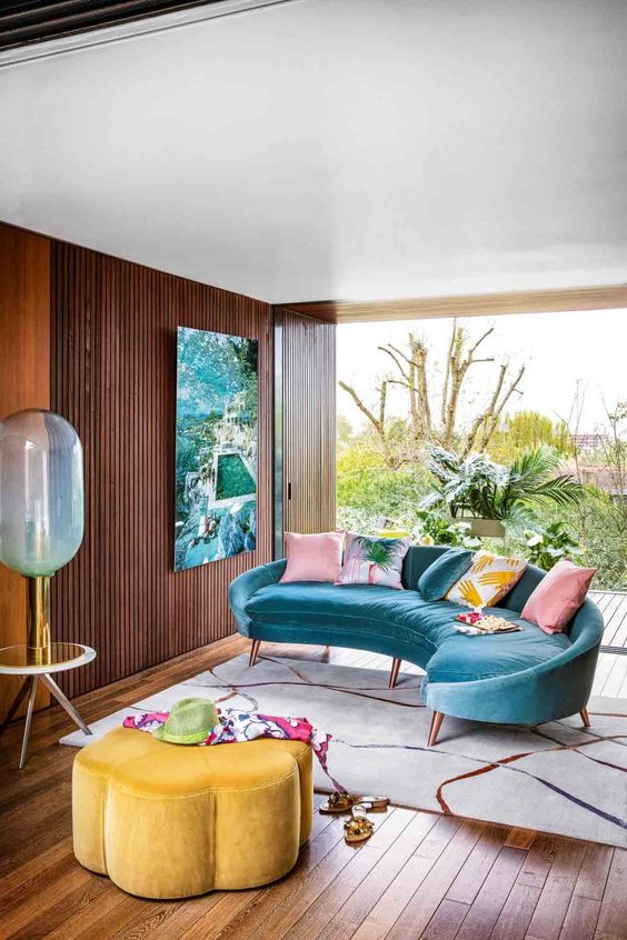 a colorful tropical living room with a bright blue curved sofa, a bright yellow flower shaped ottoman and a bold artwork