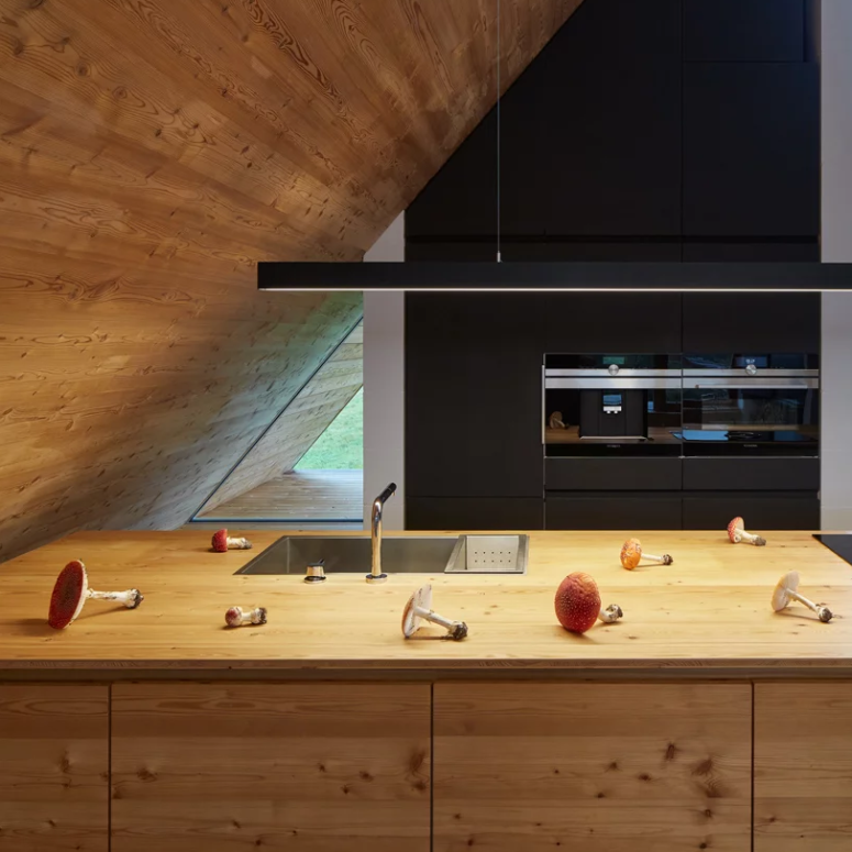 The kitchen features black cabinets, a wooden kitchen island and a simple long lamp to illuminate the space