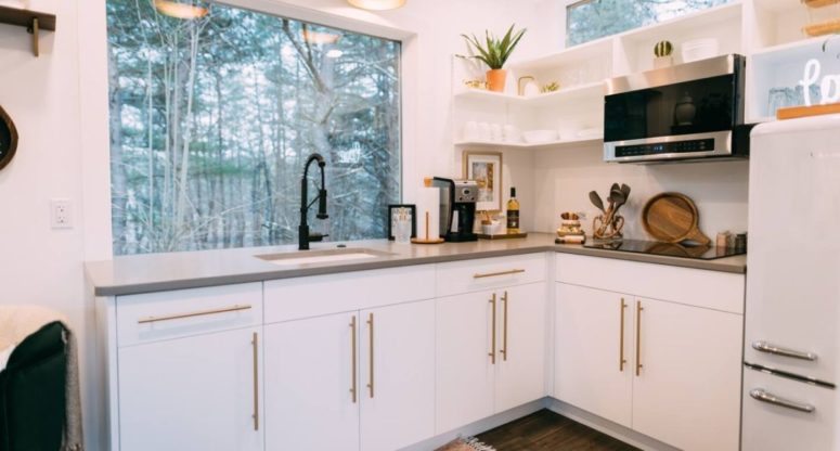 The kitchen is done with white cabinets with gold handles, there's a window to enjoy the views