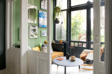 06 There’s a sunroom with bright green walls, a glazed wall, pendant lamps and plants and some cool furniture