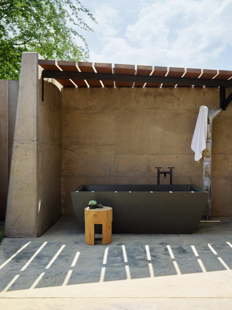 There's an outdoor bathroom with a blakc stone tub, wooden furniture and some greenery