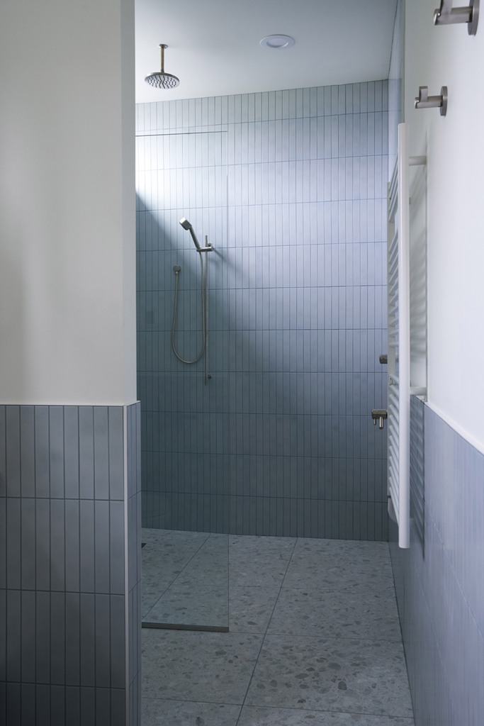The bathroom is grey amd whoite, with long and thin tiles and a terrazzo floor