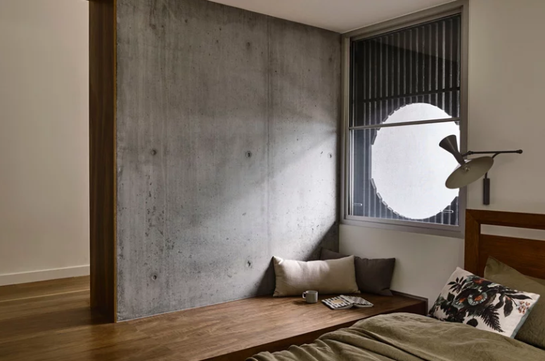 The bedroom features a bed and a platform that shapes a wooden daybed, a window made round with a bamboo screen