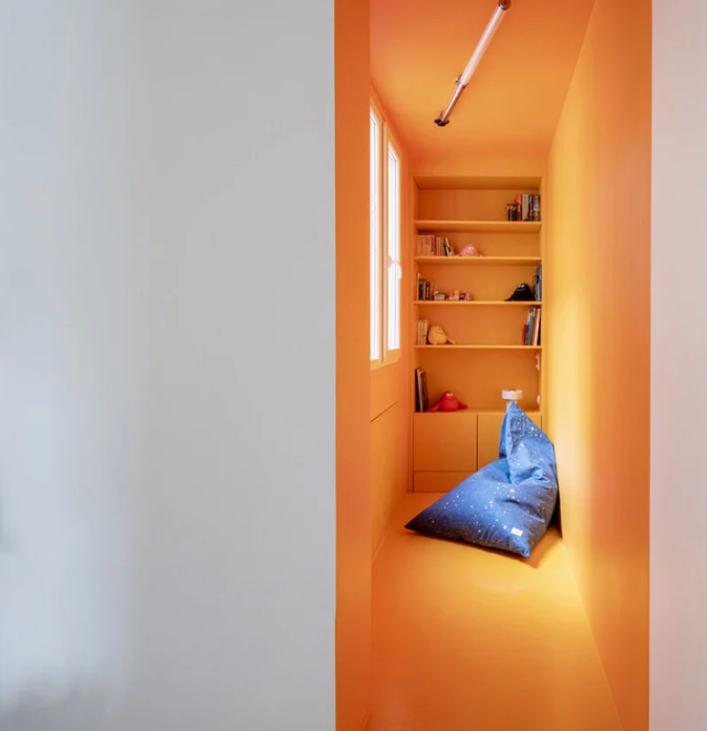 There's a kids' reading nook with bright plywood walls and built-in shelves