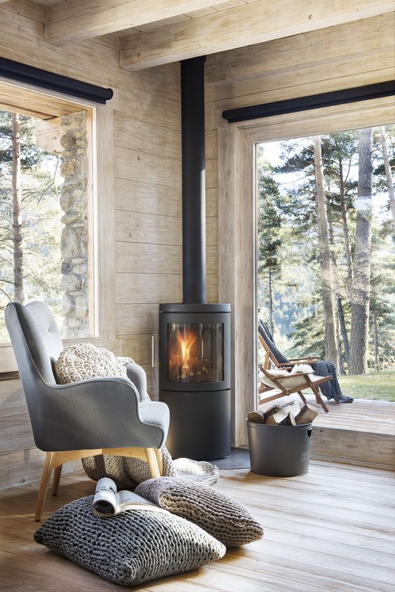 A contemporary cabin space with large windows, wood clad space and a modern wood burning stove in the corner