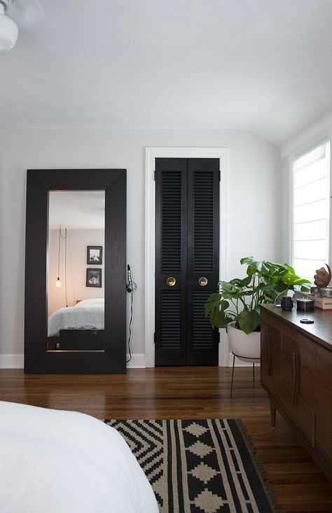 a black shutter door to the closet echoes with a dark wooden frame of the mirror and a printed rug