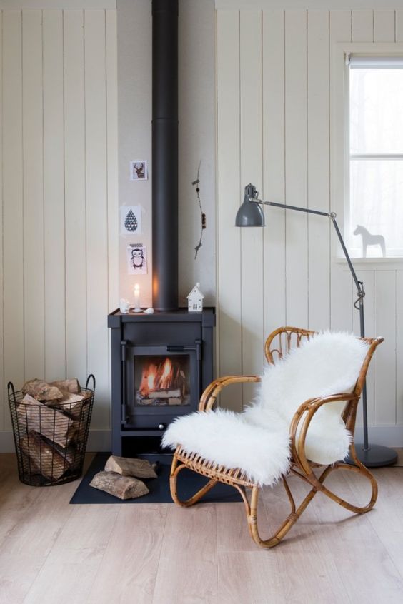 a cozy Nordic nook with wood clad walls and a black wood burning stove plus a wire basket with firewood
