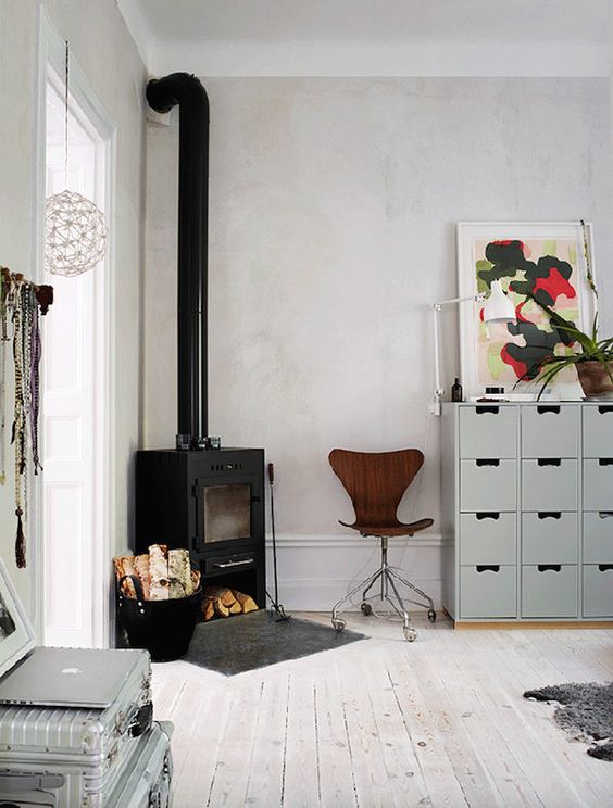 a Scandinavian room with a cozy wood bruning stove in the corner and some firewood next to it