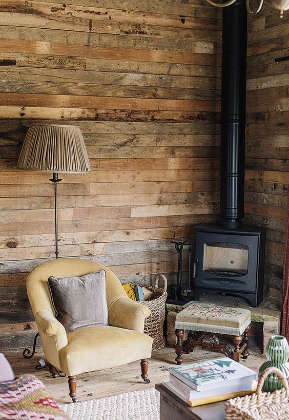 A vintage meets rustic reading nook with a wood burning stove, vintage furniture and reclaimed wood walls
