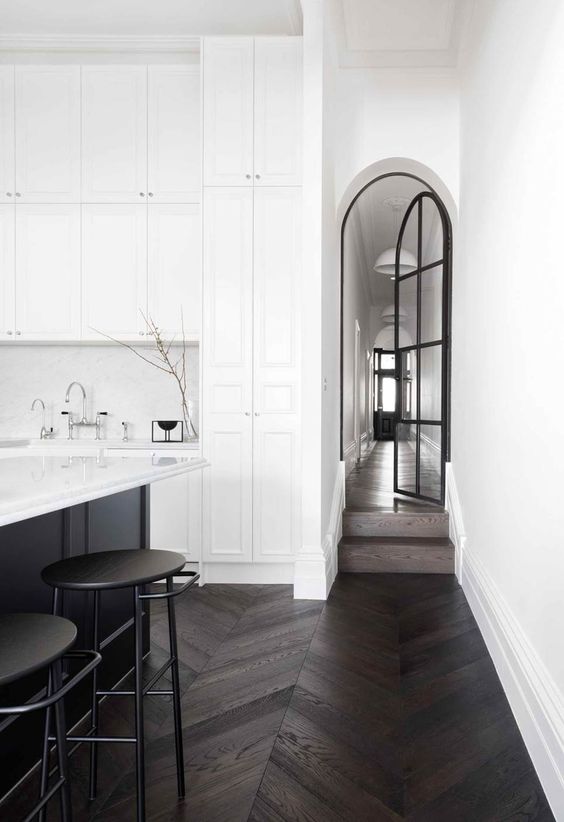 an arched black French door, a black kitchen island and stools that continue the dramatic theme of the decor