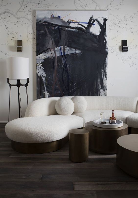 a monochromatic living room with a creamy curved sofa and round pillows and dark metal round tables