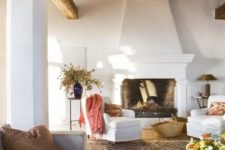 a Spanish living room with a wooden ceiling with beams, white walls and a fireplace, neutral furniture and dried blooms