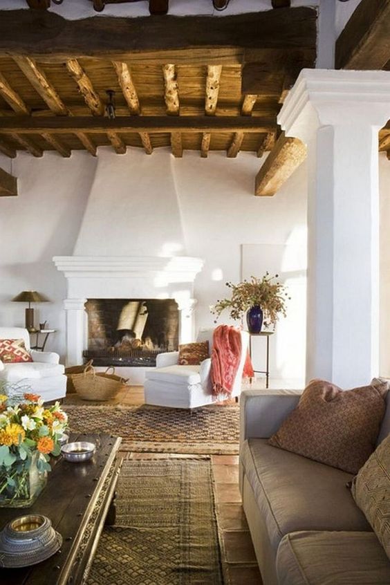 a Spanish living room with white plaster walls, wooden ceiling with beams, layered rugs and some fresh and bright accents