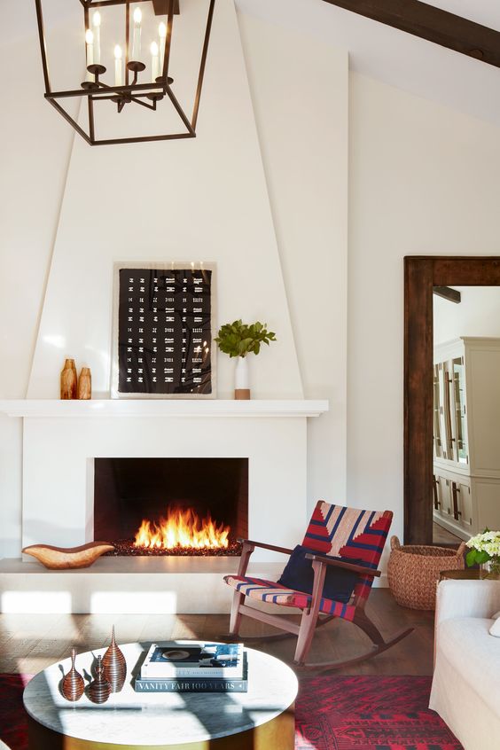 a Spanish living room with white walls and a large fireplace, printed textiles in bold colors and warm-colored artworks