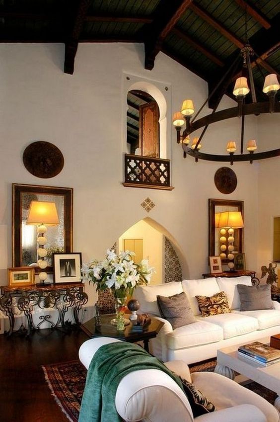 A Spanish styled room with white walls, arched doorways, neutral furniture, vintage lamps and chandeliers