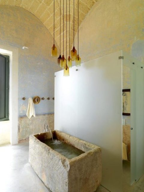 a beautiful bathroom with a rough stone bathtub and a cluster of amber glass pendant lamps