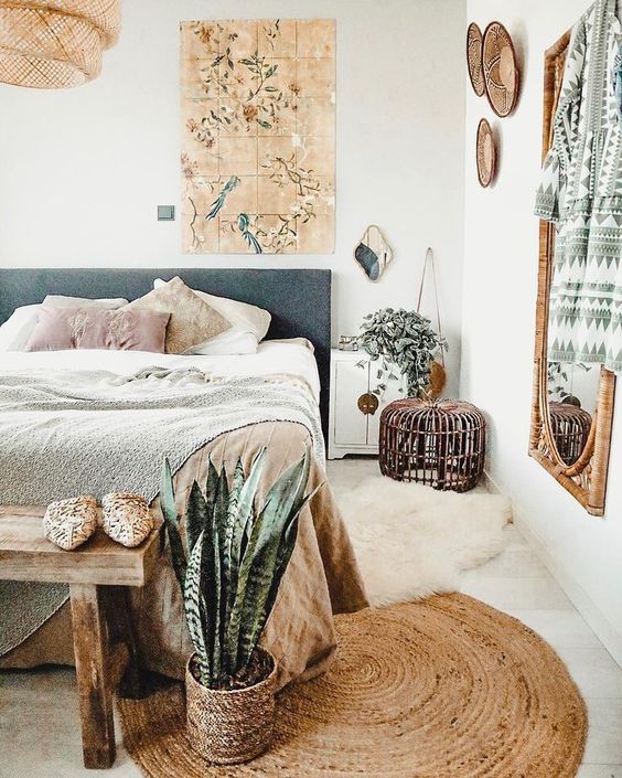 a boho bedroom with woven plates, a rattan mirror, a jute rug and a wicker lamp plus some plants