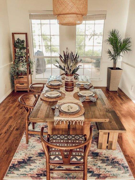 a boho dining room with a wicker lamp, reclaimed wood furniture, a boho rug and potted greenery plus macrame and wicker