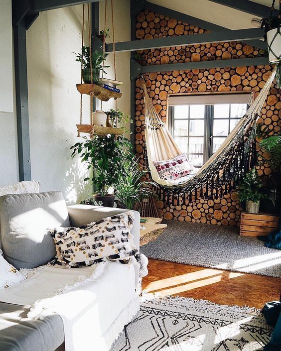 a boho space with a neutral color palette, a wood slice wall, a hammock, layered rugs and lots of greenery