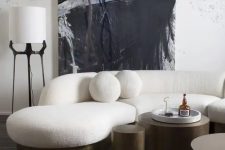 a bold and catchy living room with a white curved sofa with round pillows, metal tables, an abstract artwork and some lamps