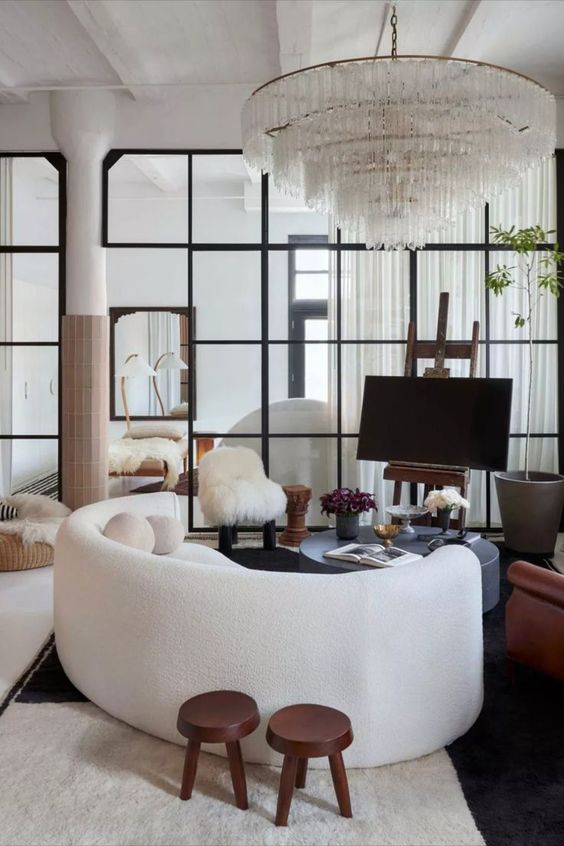 a bold living room with a white curved sofa, a grey round coffee table, a large and heavy crystal chandelier and some decor