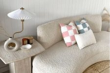 a boucle curved sofa with printed pillows, a stone side table, some candles, a vase and a quirky lamp