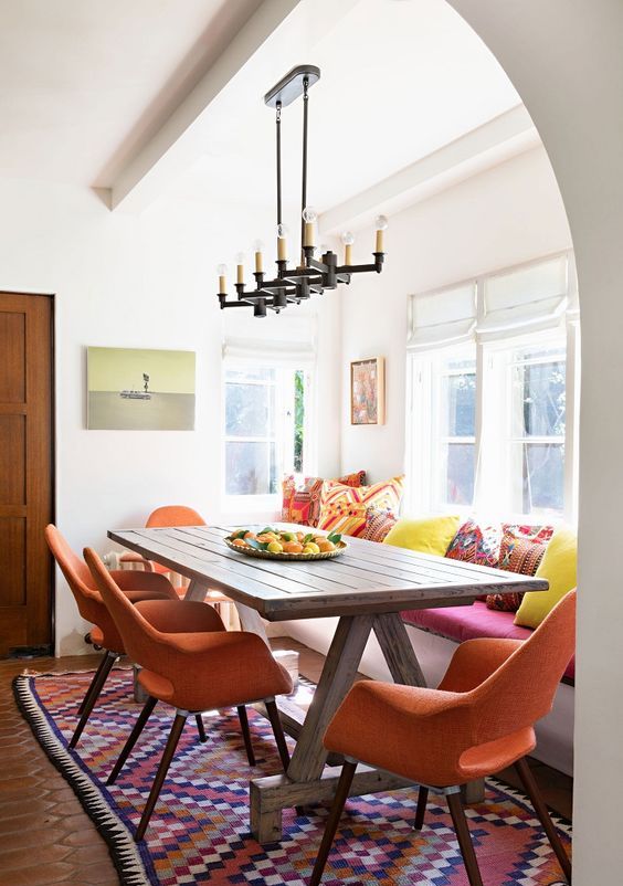 a bright and modern dining space in a Spanish space, bright pillows, warm-colored chairs, a wooden table and a vintage chandelier