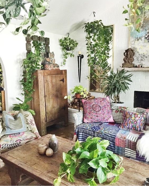 a bright boho living room with patchwork textiles, lots of potted greenery, rustic wooden furniture and a fireplace