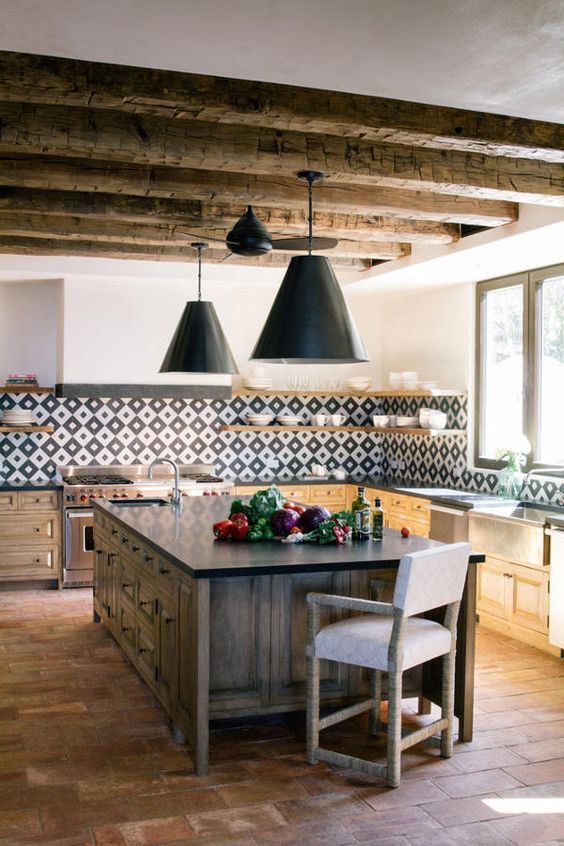 a bright modern Spanish kitchen with wooden beams, a printed tile backsplash, pendant lamps and a heavy wooden kitchen island