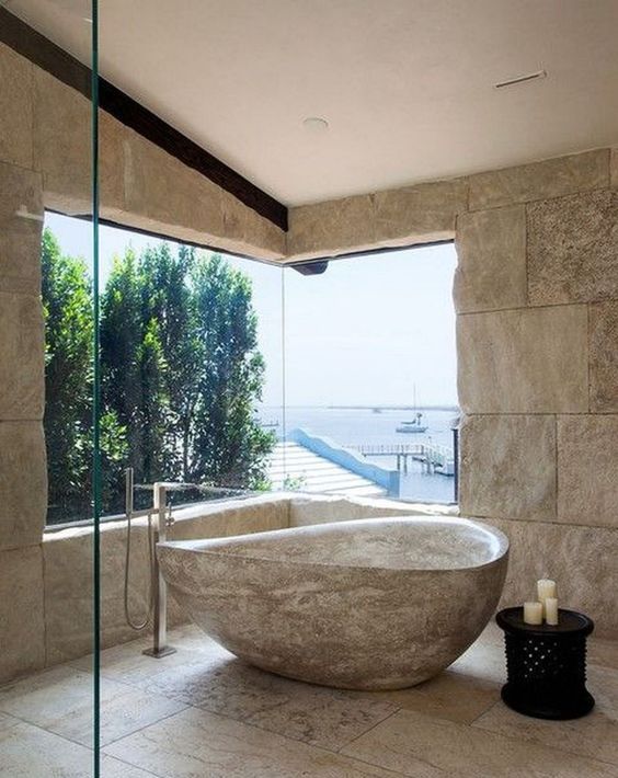 a catchy bathroom with a sea view, stone walls, stone tiles on the floor and a catchy stone bathtub