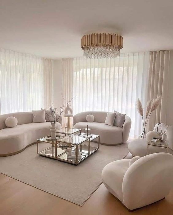 a chic all-neutral living room with curved boucle furniture, coffee tables, a crystal chandelier and some decor