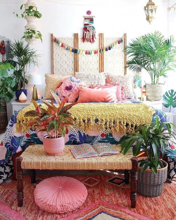 a colorful boho bedroom with all bright textiles and linens, lots of potted plants, a colorful tassel garland and Moroccan lamps