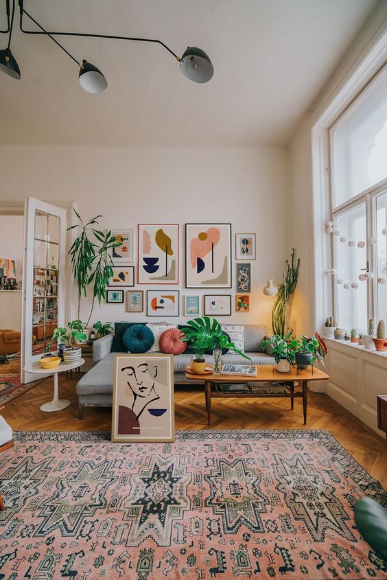 A colorful boho meets mid century living room with a bright gallery wall, a printed rug and colorful pillows plus greenery
