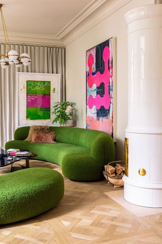 a colorful living room with a green curved sofa and ottoman, a hearth, bold artwork, a chandelier and a coffee table