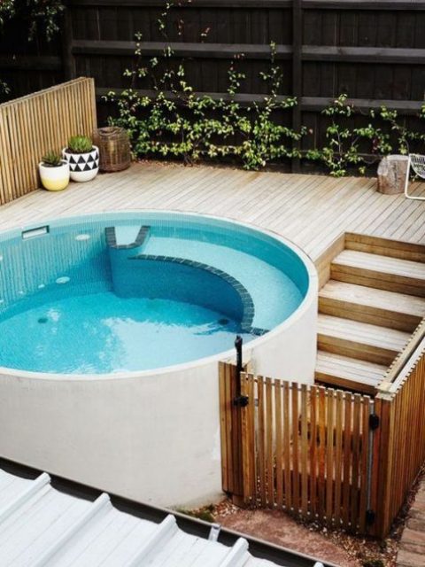 a contemporary round pool with a light-colroed wooden deck and some potted plants to make the space fresh