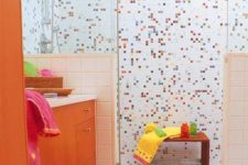 a cool colorful kids’ bathroom with mosaic tiles in the shower space and an orange vanity is all the fun and cheerfulness