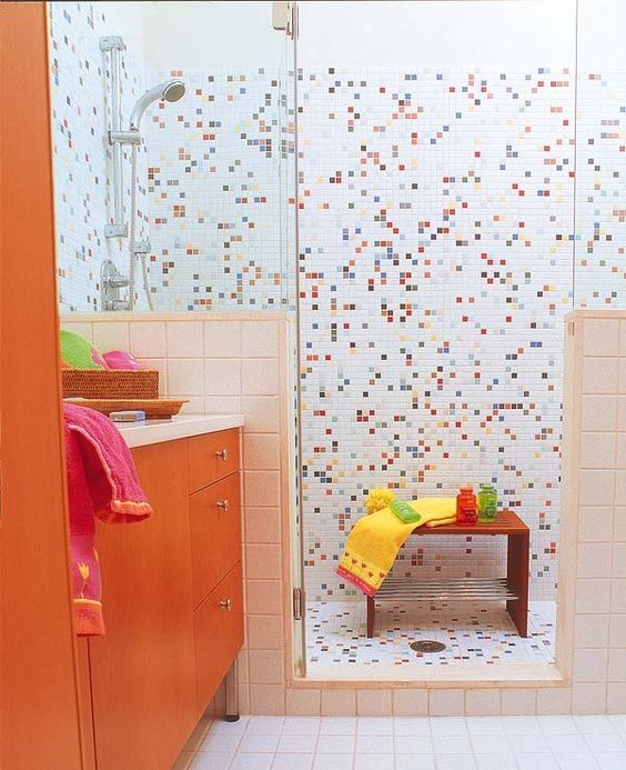 a cool colorful kids' bathroom with mosaic tiles in the shower space and an orange vanity is all the fun and cheerfulness