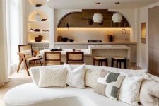 a gorgeous neutral refined space with a white boucle curved sofa, a coffee table, a dining zone and kitchen and niches with decor