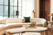 a light-filled living room with a parquet floor, a curved neutral sofa, a coffee table and a stool and some lamps