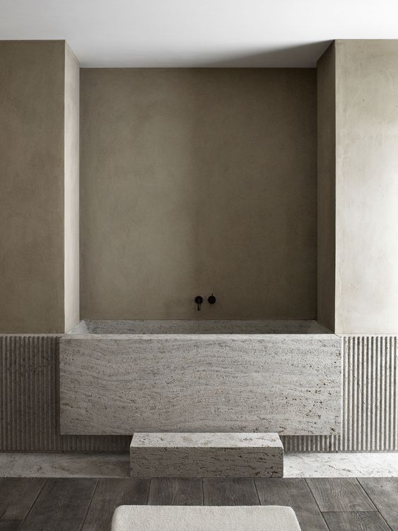 a minimalist bathroom done in neutrals, with a built-in stone bathtub and dark wooden floor