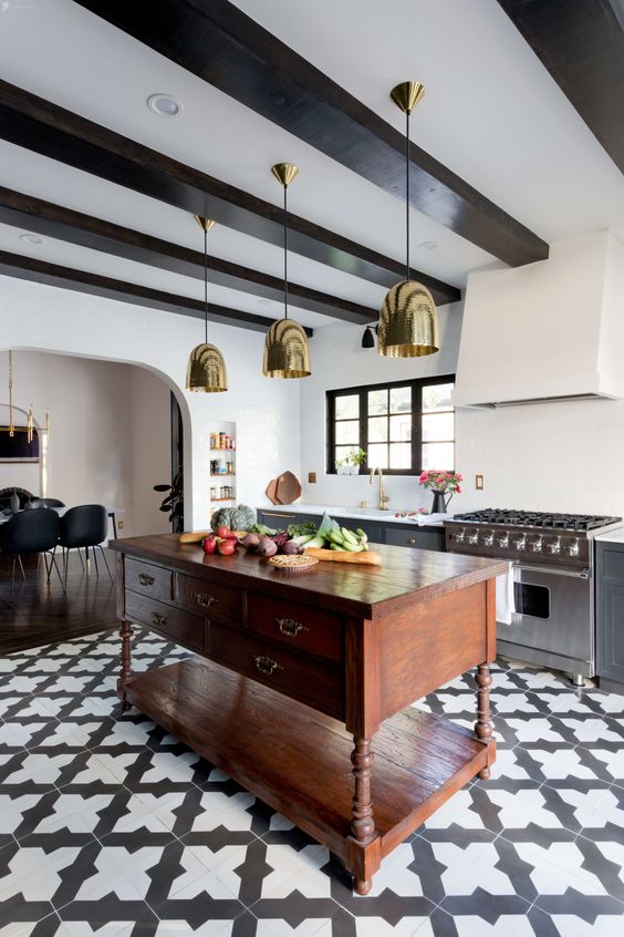 a modern Spanish kitchen with printed tiles, gold pendant lamps, heavy wooden furniture and dark wooden beams