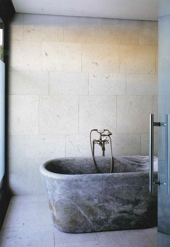 a neutral bathroom with textural tiles on the walls and floor, a grey stone bathtub and dark metal fixtures