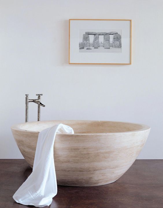 a neutral contemporary bathroom with a bowl-like stone bathtub and a catchy artwork for a modern feel