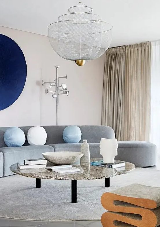 a neutral living room made bold with a curved grey sofa, a navy artwork and a marble coffee table and a cork stool