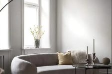a neutral minimalist living room with a curved sofa, a pendant lamp, a coffee table, pillows and blooms in a vase