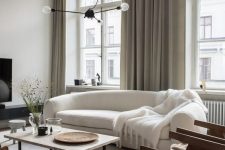 a refined Scandinavian living room with a curved white sofa, rattan chairs, a low coffee table, a pendant lamp and books