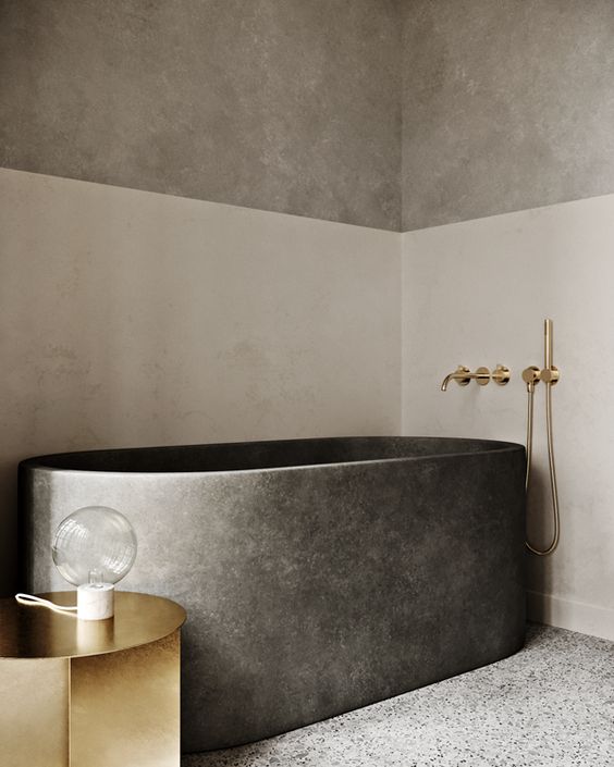 a refined and minimalist bathroom with color block walls, a stone bathtub and a polished gold side table and fixtures